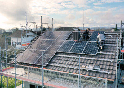 Mathias Grässl und Martin Salzmann von Soleis AG installieren ein Solarpanel auf einem Schrägdach im Sonnenschein.