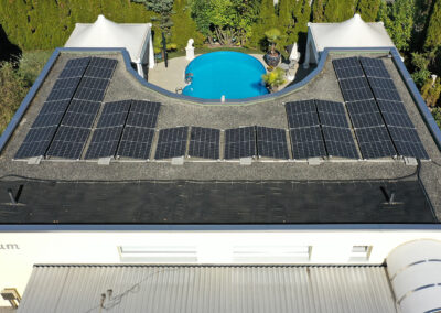 Solarpanels auf Flachdach, im Hintergrund Berge, Bäume und Häuser