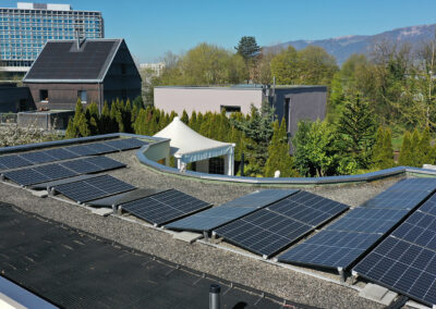 Solarpanels auf Flachdach, im Hintergrund Berge, Bäume und Häuser