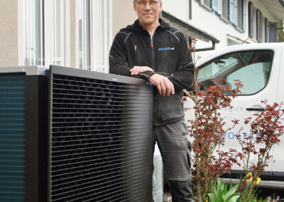 Wärmepumpe aussen vor einem Haus. Daneben Mathias Grässl von Soleis AG.