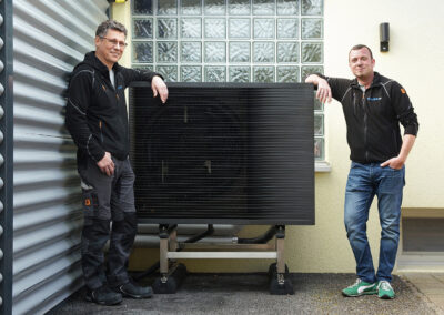 Zwei Männer stehen neben einer Wärmepumpen aussen vor einem Haus
